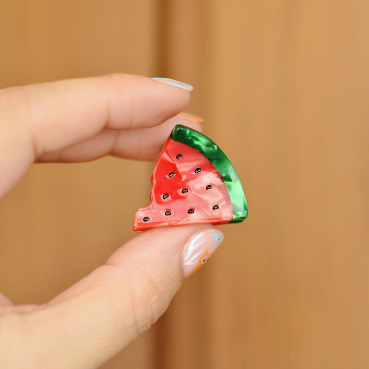 Hand holding a small watermelon hair claw clip against a wooden background