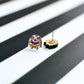 A small Mr Blobby stud earring featuring his face and bow tie, shown next to the other earring from the pair placed upside down to reveal the earring post on the back.