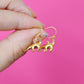 Gold plated brontosaurus shaped earrings with hooks, held by a hand against a pink background
