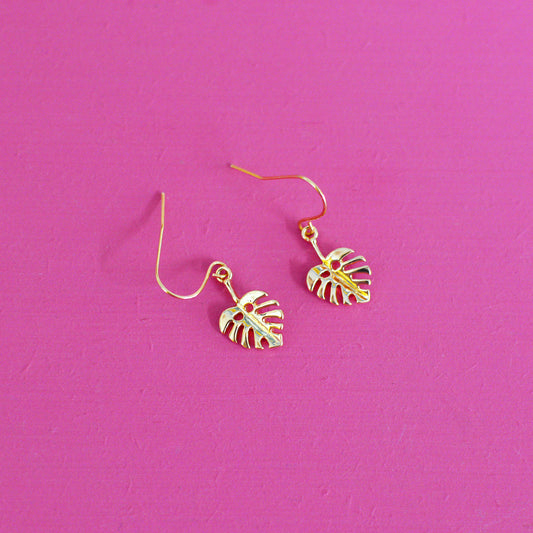 Gold leaf shaped earrings with hooks on a pink background
