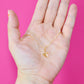 Gold plated necklace with a leaf pendant held in a hand against a pink background