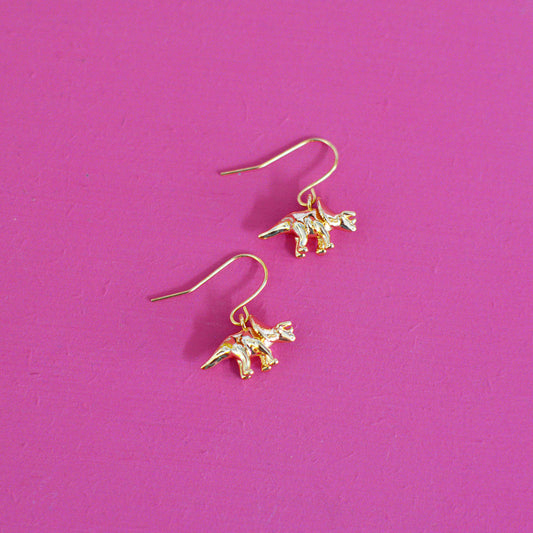 Gold plated triceratops dinosaur earrings with hooks on a pink background