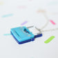 A super close up image of a typewriter pendant laying on it's side so you can see that is is made up of two layers of blue acrylic.