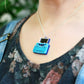 A close-up lifestyle shot of a person wearing a silver chain necklace with a miniature blue retro typewriter pendant